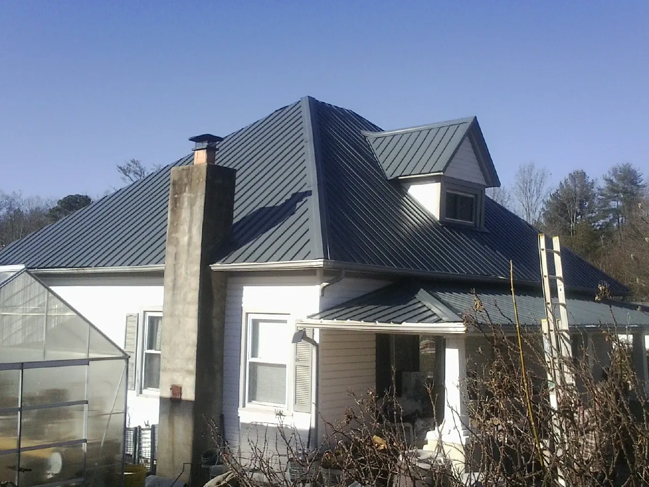 Dark blue standing seam metal roof on a white farmhouse with dormer — Slate & Tile Roof Repair by Roofing Brothers in De Pere