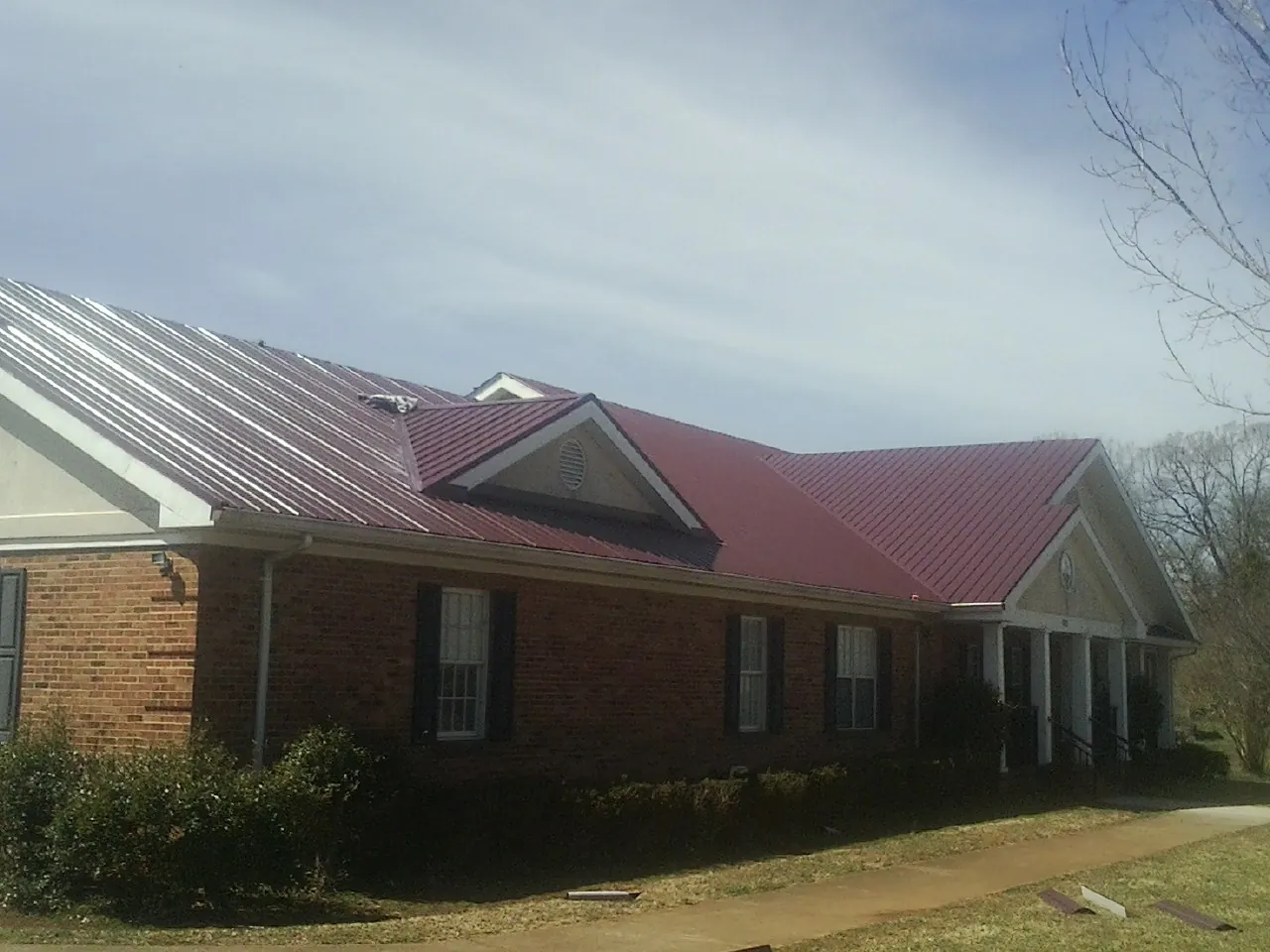 Red metal roof with gabled entries on a long brick building, from a Hail Damage Roof Repair job in De Pere