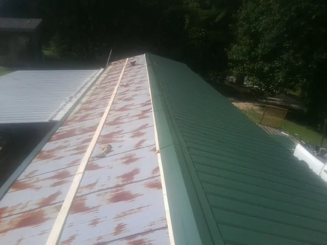 Old rusted panels beside newly installed green metal roofing — Wind Damage Roof Repair by Roofing Brothers in De Pere