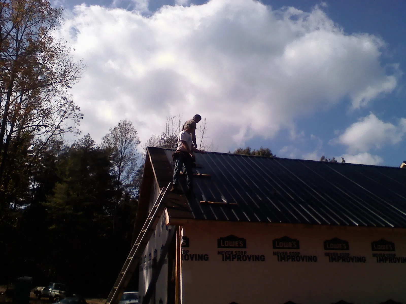 Roofer fastening dark metal panels high against a cloudy sky, from a Roof Inspection job in De Pere