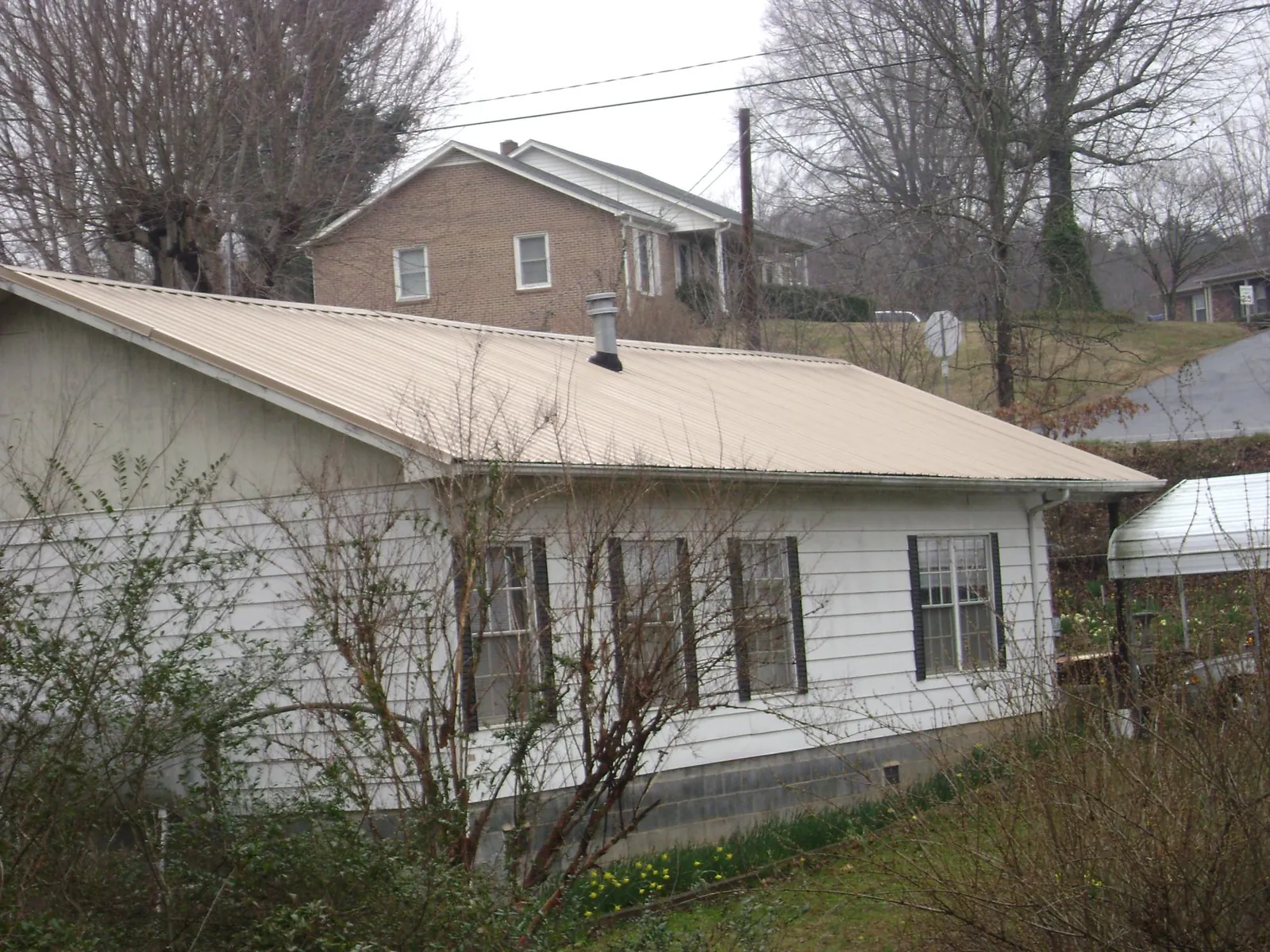 Tan metal roof on a white sided house set into a hillside — Commercial Roofing by Roofing Brothers in De Pere